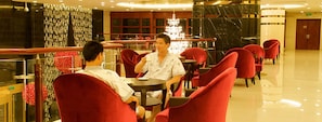 Un vestíbulo de hotel con sillas rojas, una araña de cristal y suelo de mármol.