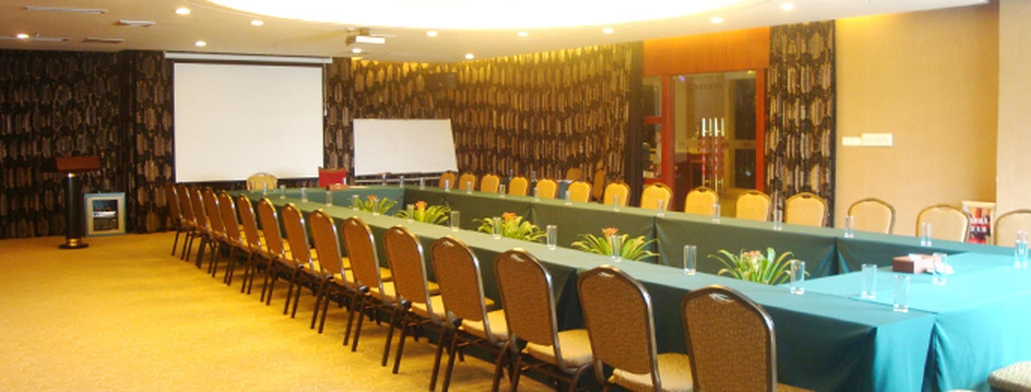 A conference room with a long table, chairs, a projector screen, and a carpeted floor.