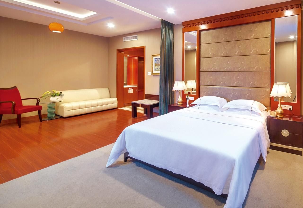 A hotel room with a large bed, a sofa, a chair, a desk, and a mirror.
