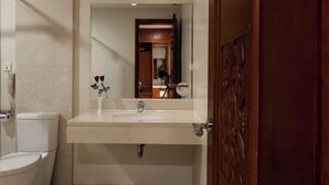 Un baño con inodoro blanco, lavamanos con espejo y puerta de madera.