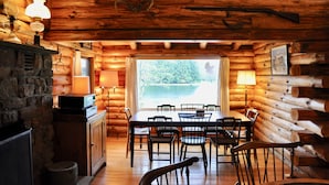 A log cabin interior with a dining area, stone fireplace, and a view of a lake. - Spruce Lake Farm 56-acre mountain-top log home estate on private 7-acre lake (Bovina)