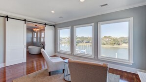 A spacious room with a large window overlooking a body of water, a built-in bench, and a modern light fixture. - 20 Morgan Place Drive by AvantStay | Waterfront Home w/ Private Dock (Isle of Palms)