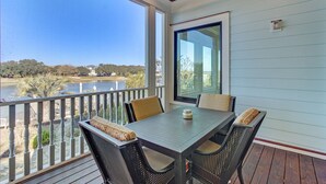 A balcony with a table and chairs, overlooking a body of water and a golf course. - 20 Morgan Place Drive by AvantStay | Waterfront Home w/ Private Dock (Isle of Palms)