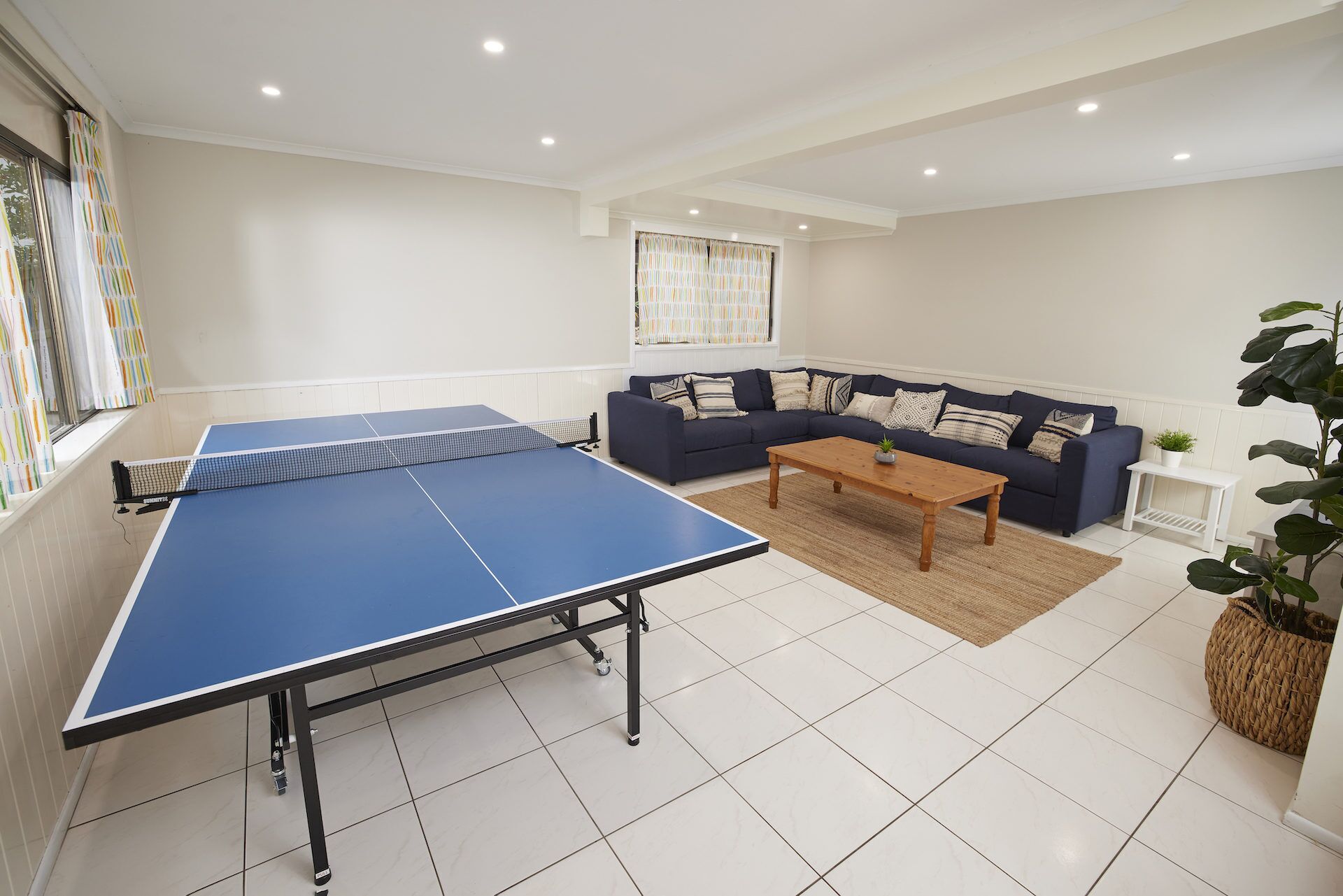 Un salon avec une table de ping-pong, un canapé bleu foncé, une table basse en bois et une plante en pot.