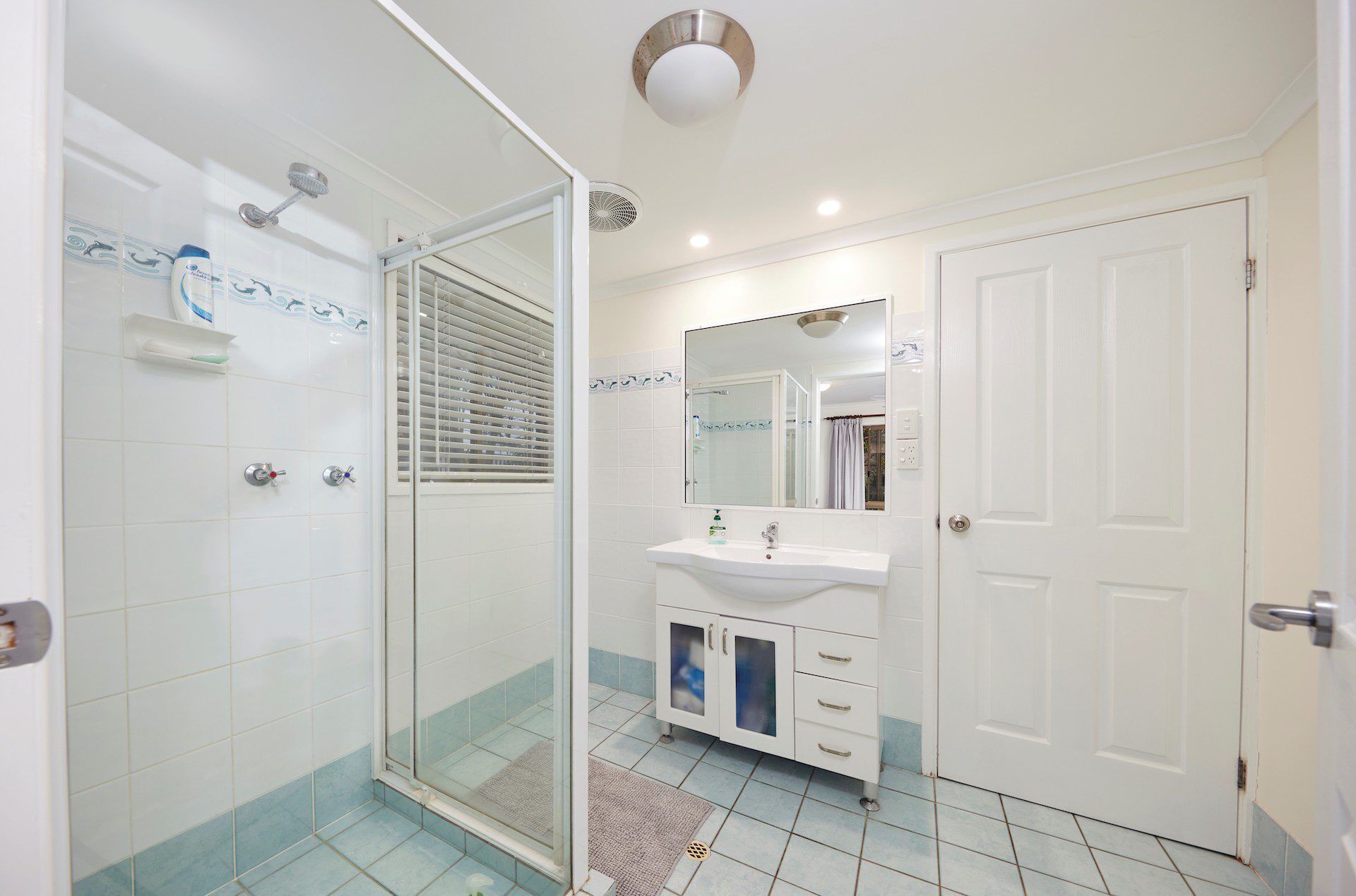 Une salle de bain avec une douche à parois de verre, un lavabo blanc avec un miroir et une porte.