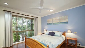 Une chambre à coucher avec un lit en bois, un ventilateur de plafond, une grande fenêtre avec des rideaux et deux lampes de chevet.