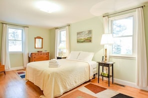 A well-lit bedroom with a large bed, a dresser, a nightstand, and a painting on the wall.