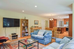 A living room with a television, a bookshelf, a blue sofa, a coffee table, and a dining area with wooden furniture.