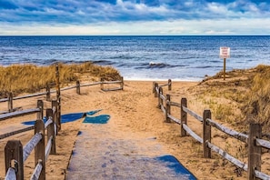 A beach with a wooden walkway leading to the sea, a sign reading "KEEP OFF THE DUNES", and a clear view of the ocean.