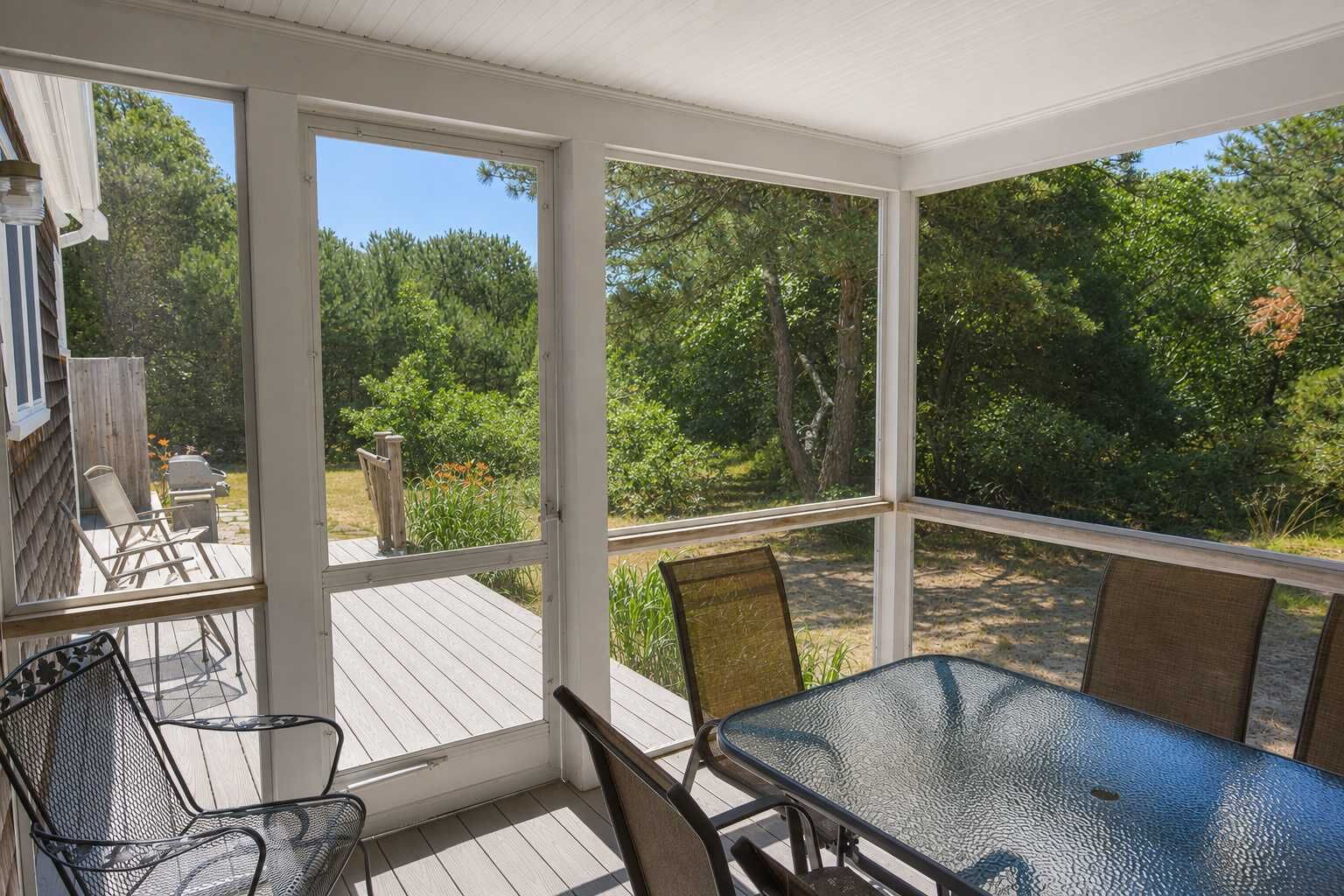 Un patio cubierto con mesa y sillas, con vista a un jardín con árboles y una terraza de madera.