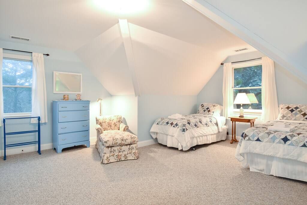 Ein Schlafzimmer mit schrägem Dach, zwei Betten, einer Kommode, einem Stuhl und einer Lampe.