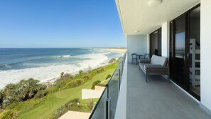 A balcony with a view of the ocean, a seating area with a sofa and chairs, and a glass door leading to the interior. - Edgecliffe Unit 7, 4 Bulcock Beach Esplanade Kings Beach (CALOUNDRA)