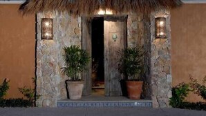 Une construction à toit de chaume, avec des murs en pierre et des plantes en pot, qui ressemble probablement à une maison d’hôtes ou à une chambre privée.