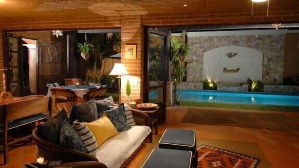Un salon chaleureux avec un canapé, des poufs et une table basse. On aperçoit une piscine à travers les portes vitrées.