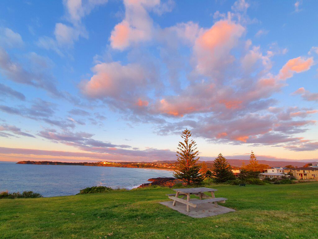 Ein Picknicktisch in einer grünen Wiese mit Blick auf das Meer und einen Sonnenuntergang.