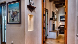 A hallway with wooden flooring, a framed painting of a cow, and a wooden beam ceiling. - Casa Sanchez | Modern Pueblo-Style Retreat (Santa Fe)