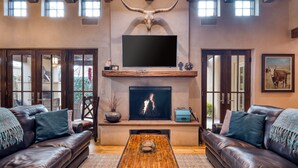 A living room with leather sofas, a wooden coffee table, a fireplace, and a mounted TV. - Casa Sanchez | Modern Pueblo-Style Retreat (Santa Fe)