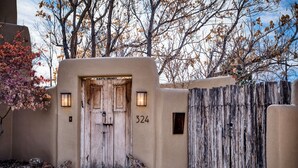 A rustic entrance with a wooden door, numbered 324, and a wooden fence. - Casa Sanchez | Modern Pueblo-Style Retreat (Santa Fe)