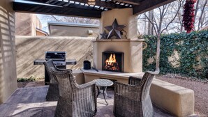 An outdoor patio with a built-in fireplace, wicker furniture, and a grill. - Casa Sanchez | Modern Pueblo-Style Retreat (Santa Fe)