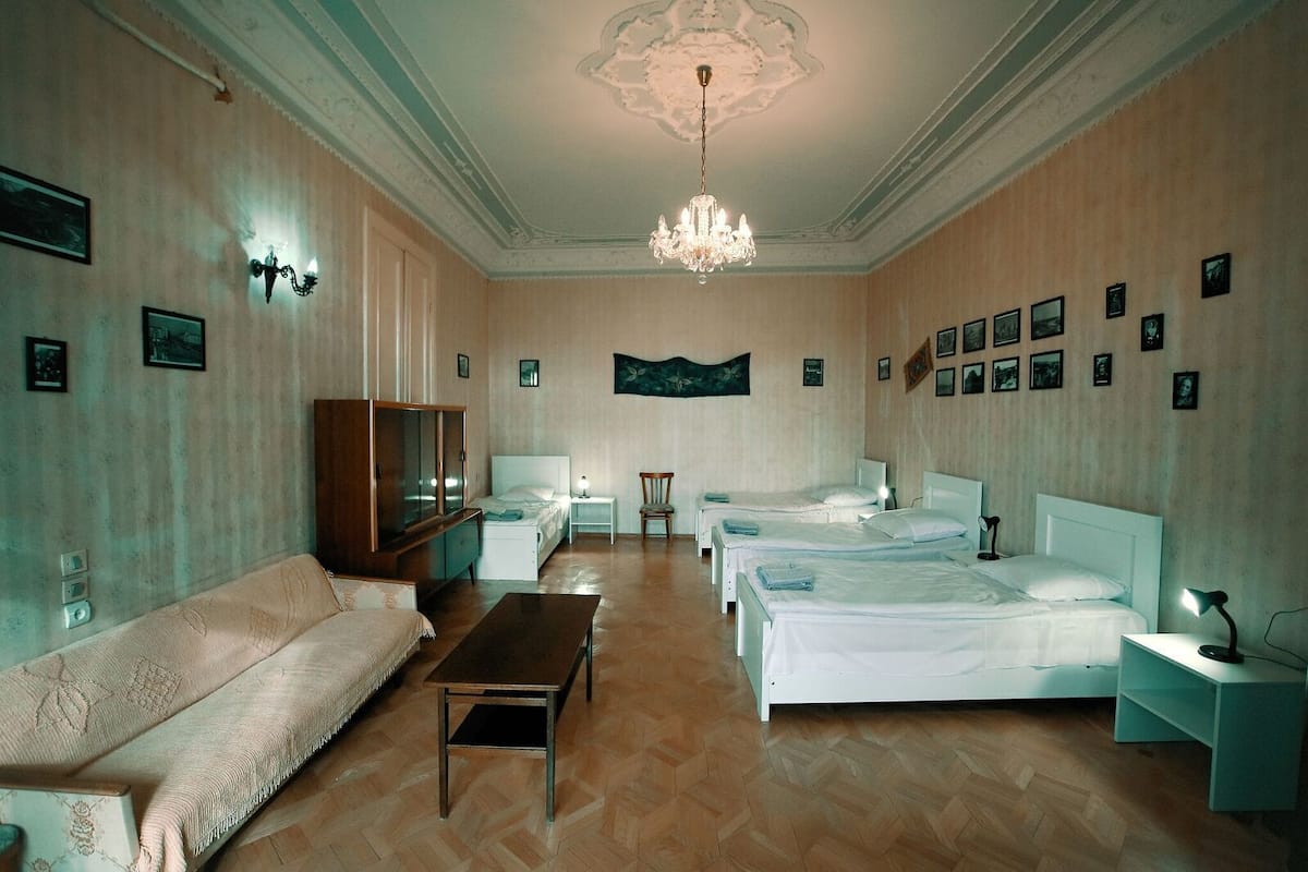 A hotel room with a large bed, a sofa, a wooden cabinet, and a chandelier.