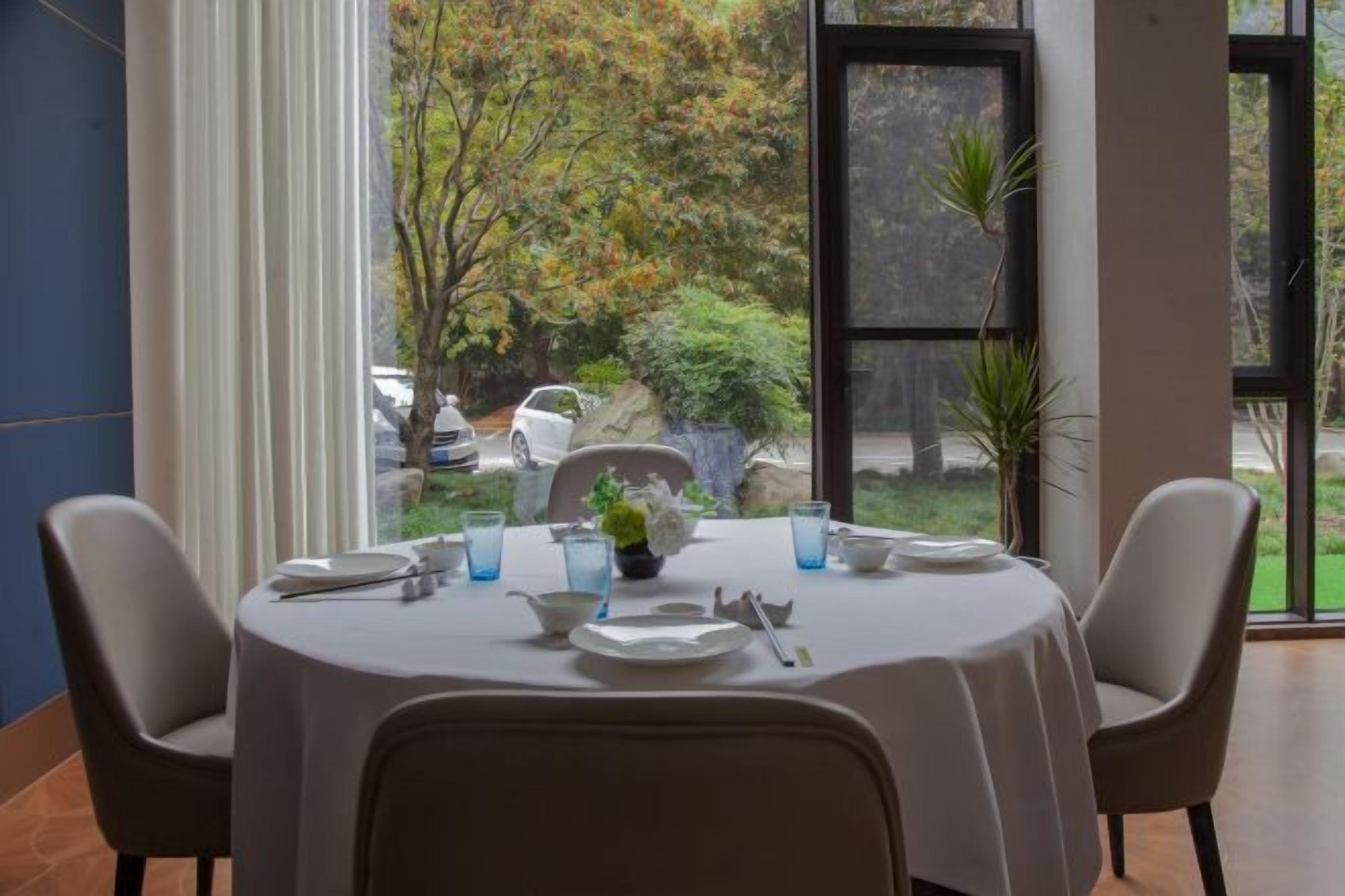 Mesa de comedor preparada para cuatro personas, con sillas, un jarrón de flores y vistas a un jardín a través de una ventana.