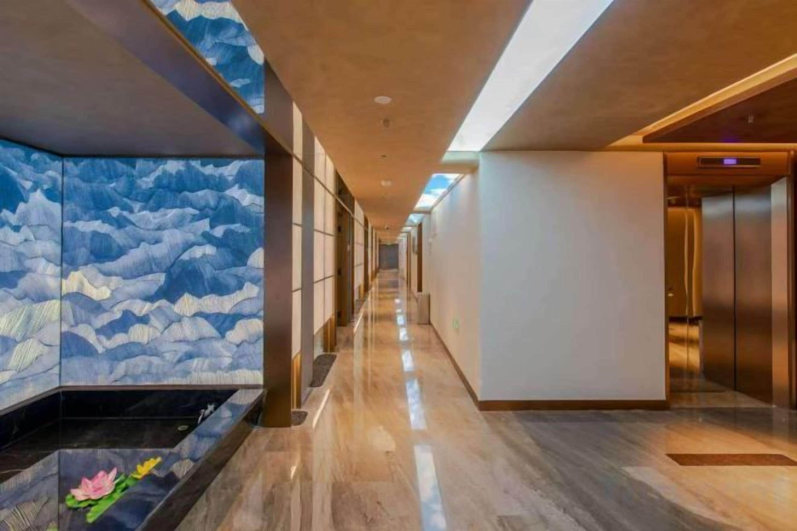 A hotel corridor with a decorative wall, a water feature, and an elevator.