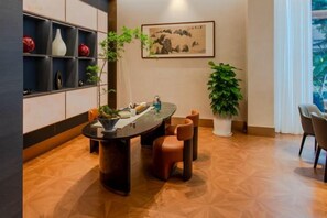 A dining area with a round table, chairs, a potted plant, and a wall-mounted painting. - Huangyan International Hotel (Taizhou)