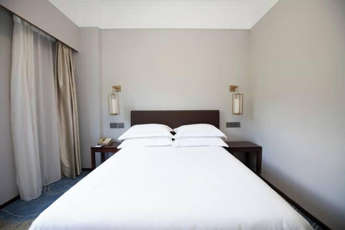 A hotel room with a large bed, two bedside tables, a telephone, and a window with curtains.