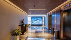 Um lobby de hotel moderno com piso de mármore polido, balcão de recepção, um grande aquário e portas de elevador.