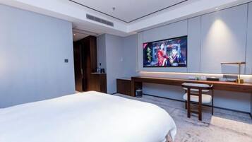 A modern hotel room with a large bed, a desk with a chair, a television, and a small table.