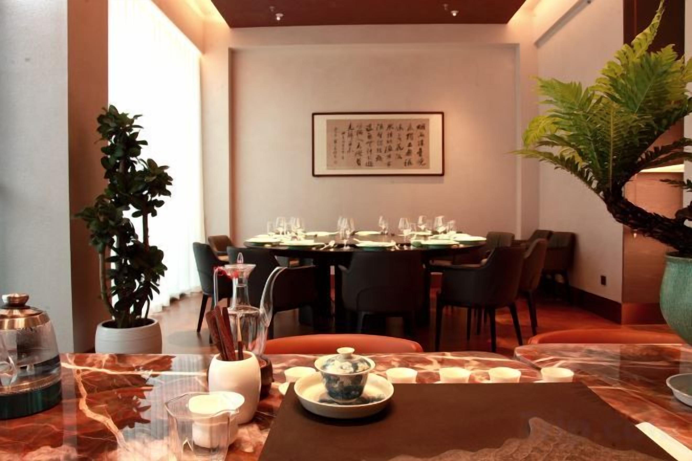 A dining area with a table set for four, chairs, a potted plant, and a framed artwork on the wall.