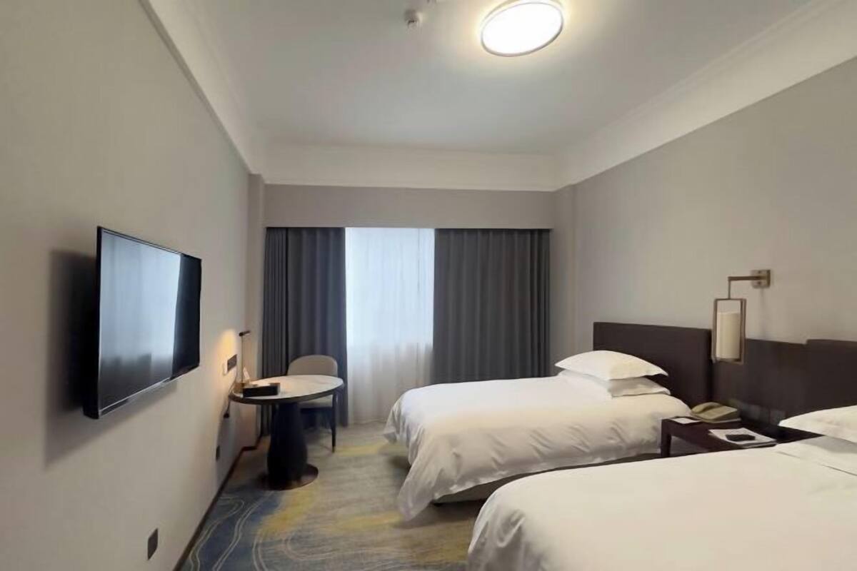 A hotel room with two beds, a TV, a desk, and a chair.