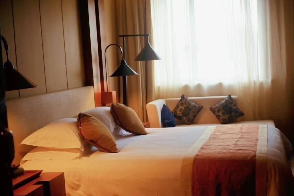 A neatly made bed with a white comforter and a red blanket, flanked by two black floor lamps and a wooden nightstand.