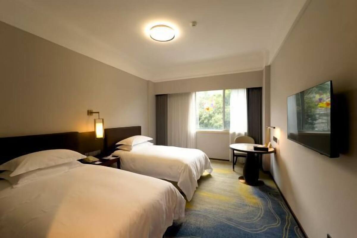 A hotel room with two beds, a desk, a chair, a TV, and a window with curtains.