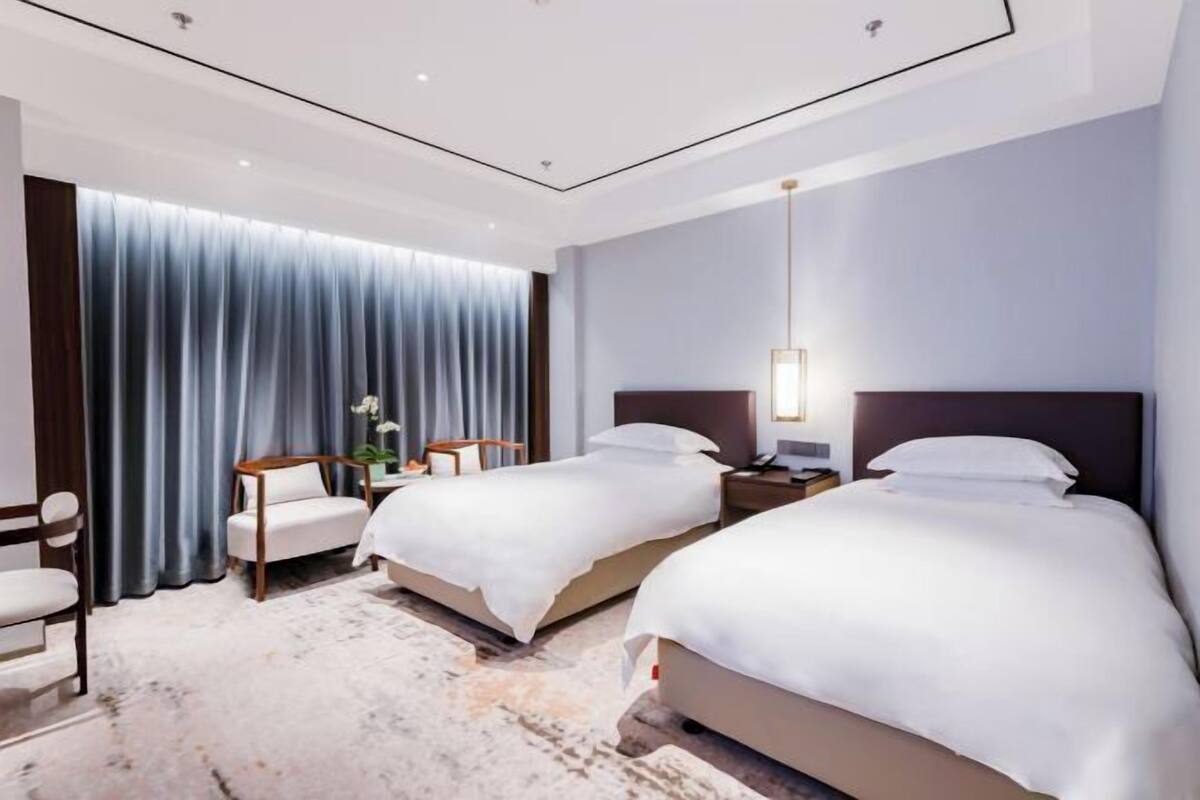 A hotel room with two beds, a desk, a chair, and a large window with curtains.