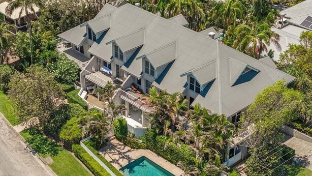 A large, multi-story house with a swimming pool and lush landscaping.