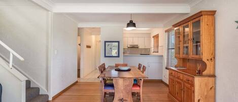 Un comedor con mesa y sillas de madera, un mueble con puertas de vidrio y una escalera a la izquierda.