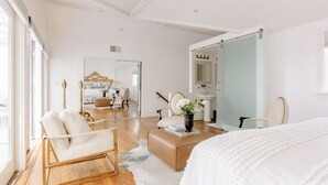 Camera da letto moderna con un letto grande, una chaise longue, una toeletta con uno specchio e vista sulla città attraverso ampie finestre.