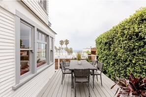 A balcony with a table and chairs, a large window, and a hedge. - Head-on OCEAN VIEW  BEACH HOUSE! (Santa Monica)