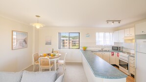 A modern kitchen with a dining area, featuring a large window, a microwave, and a refrigerator. - Intrepid, 12/3 Intrepid Close - right on the beachfront (Nelson Bay)