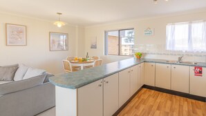 A compact kitchen with a dining area, a sofa, and a window with a view. - Intrepid, 12/3 Intrepid Close - right on the beachfront (Nelson Bay)