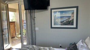 A bedroom with a bed, a television mounted on the wall, and a framed picture of a coastal landscape. - COZY PRIVATE STUDIO GUEST HOUSE. (Menifee)