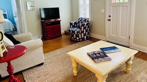 A living room with a TV, a red cabinet, a patterned armchair, a small table with a book, and a fish decoration on the wall. - Adorable, “ Beach View Cottage” Lake Michigan views! Best location!  (Ludington)