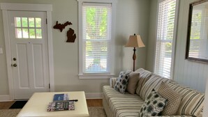 A living room with a striped sofa, a white table with magazines, and a lamp. - Adorable, “ Beach View Cottage” Lake Michigan views! Best location!  (Ludington)