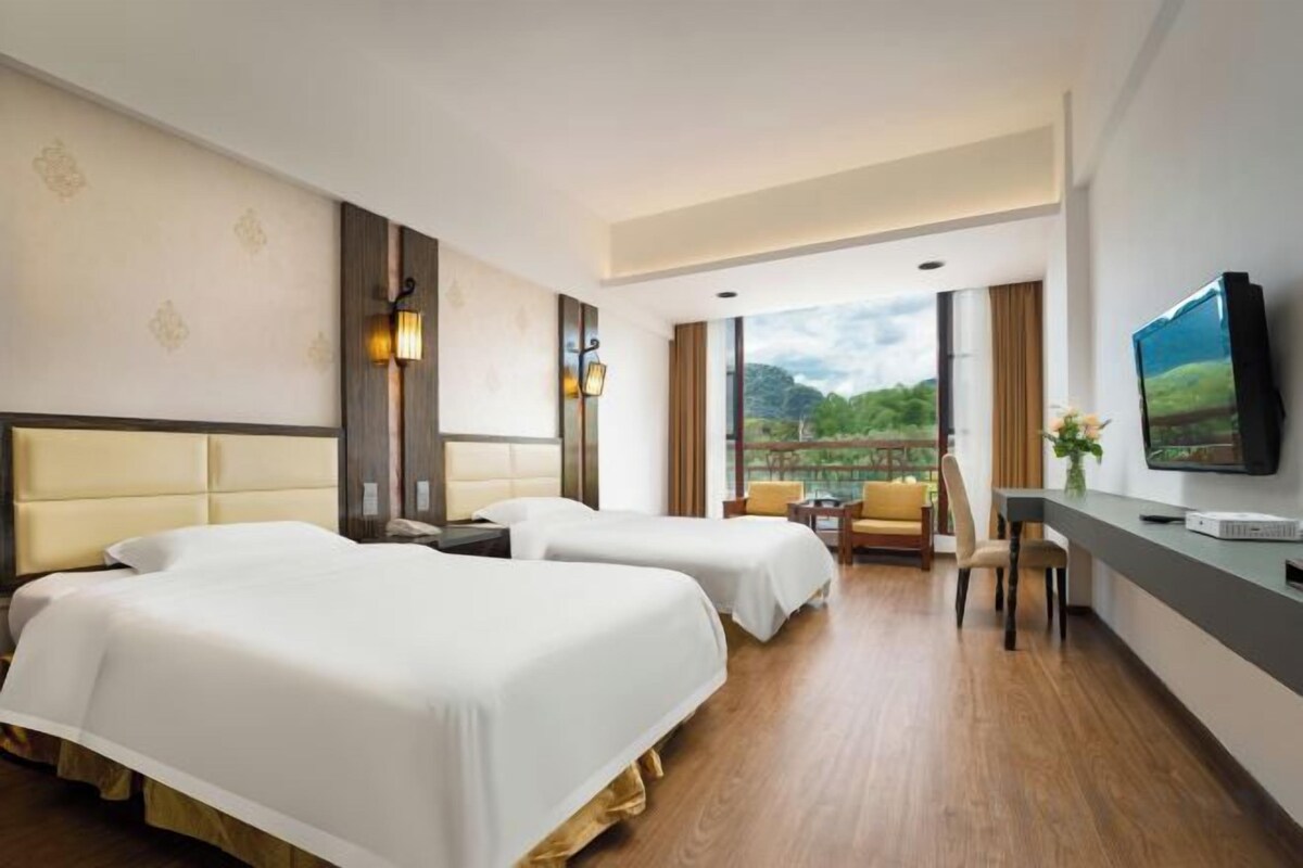 A hotel room with two beds, a desk, and a TV.