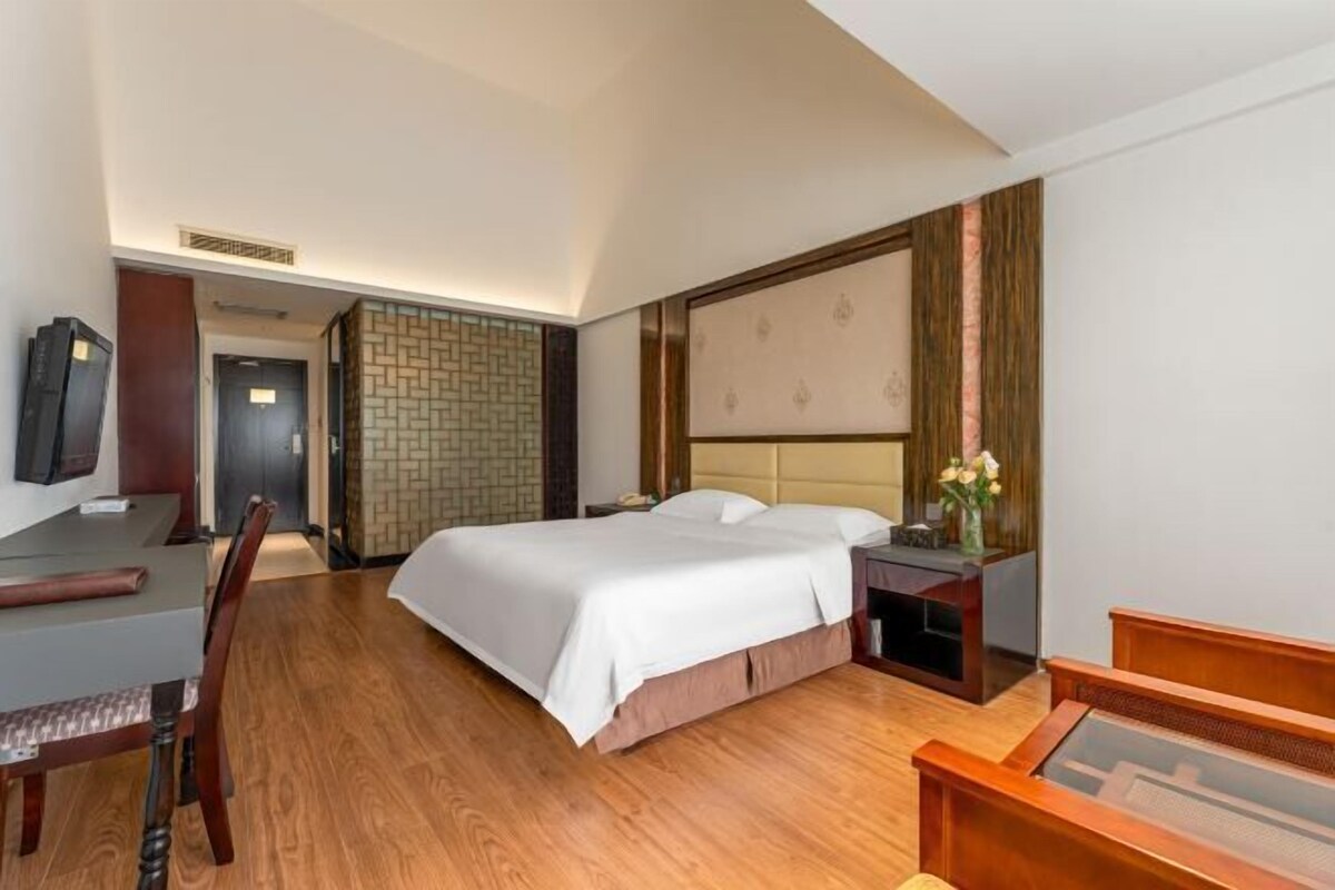 A hotel room with a bed, a desk, a chair, and a TV.