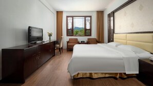 A hotel room with a bed, a TV, a desk, and a window with curtains. - Jiu Hu Shan Hotel (Zhaoping)