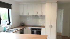 A modern kitchen with white cabinets, a wooden countertop, and a stainless steel sink. - Seabreeze Escape | Pet-Friendly Coastal Retreat | Sleeps 8 | Walk to Beach (Cape Paterson)