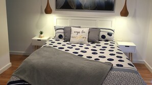 A neatly arranged bedroom with a bed, two bedside tables, a wall-mounted air conditioner, and a large abstract painting above the bed. - Seabreeze Escape | Pet-Friendly Coastal Retreat | Sleeps 8 | Walk to Beach (Cape Paterson)