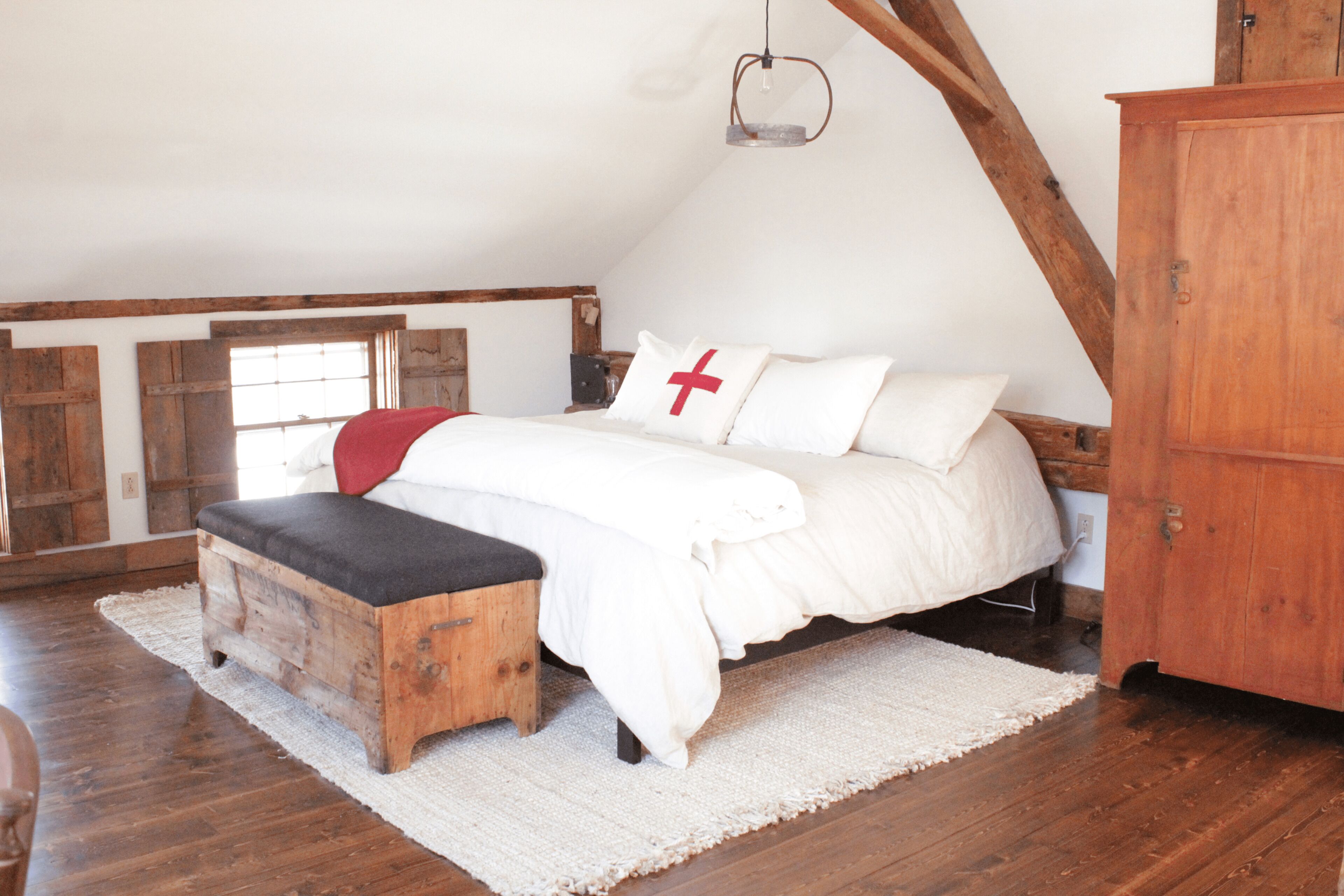 Une chambre avec un lit en bois, un banc, un tapis blanc et une armoire en bois.